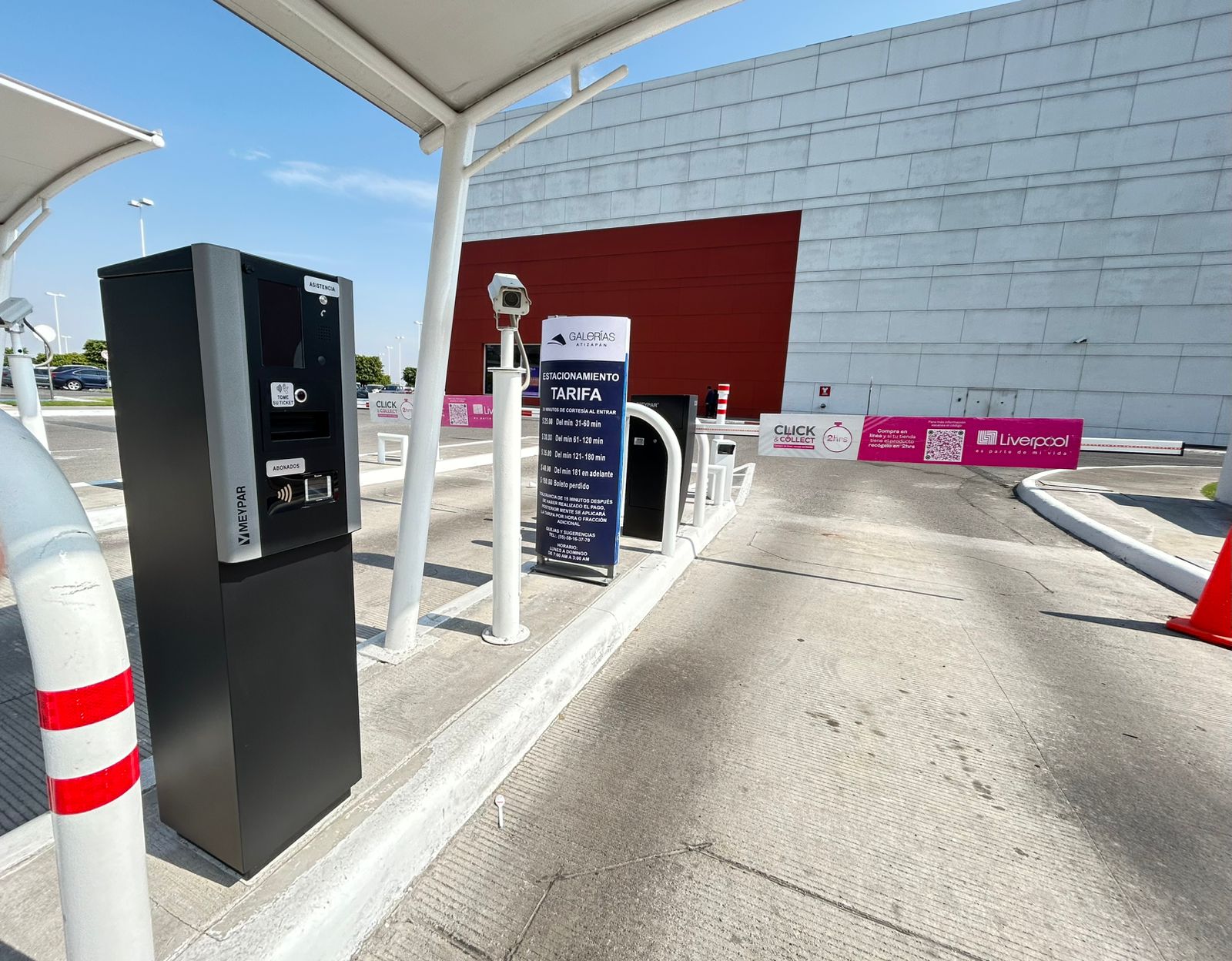 Acceso vehicular frente a centro comercial con señalización tarifaria